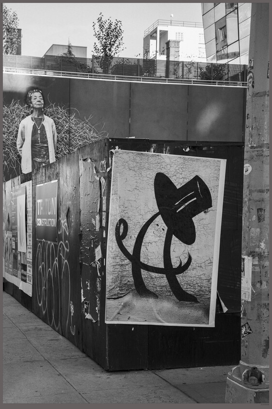 Large poster of an abstract figure wearing a top hat posted on a construction fence along a city sidewalk.