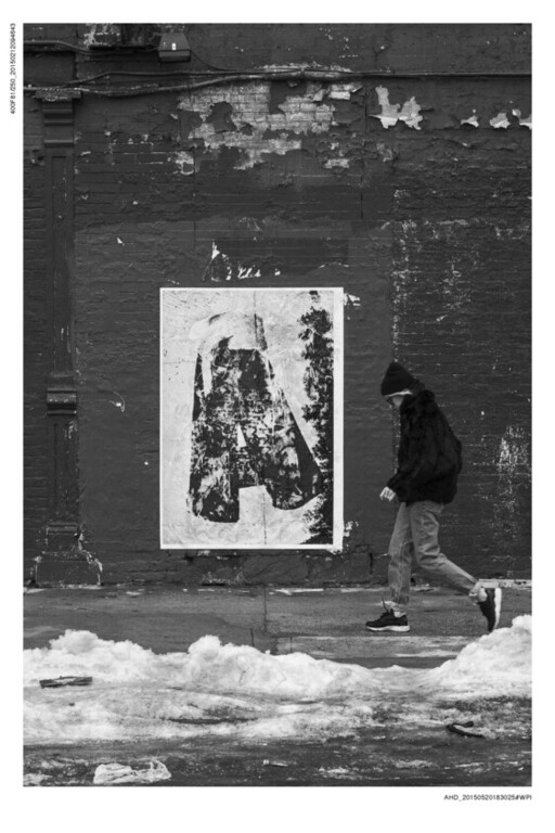 A person walks along a snowy sidewalk past a weathered poster of a large letter A on a wall.