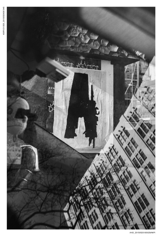 A black and white photograph with a complex, layered composition that includes a silhouette of a person painted on a wall, overlaid with reflections of trees and buildings, creating a dreamlike, abstract scene.