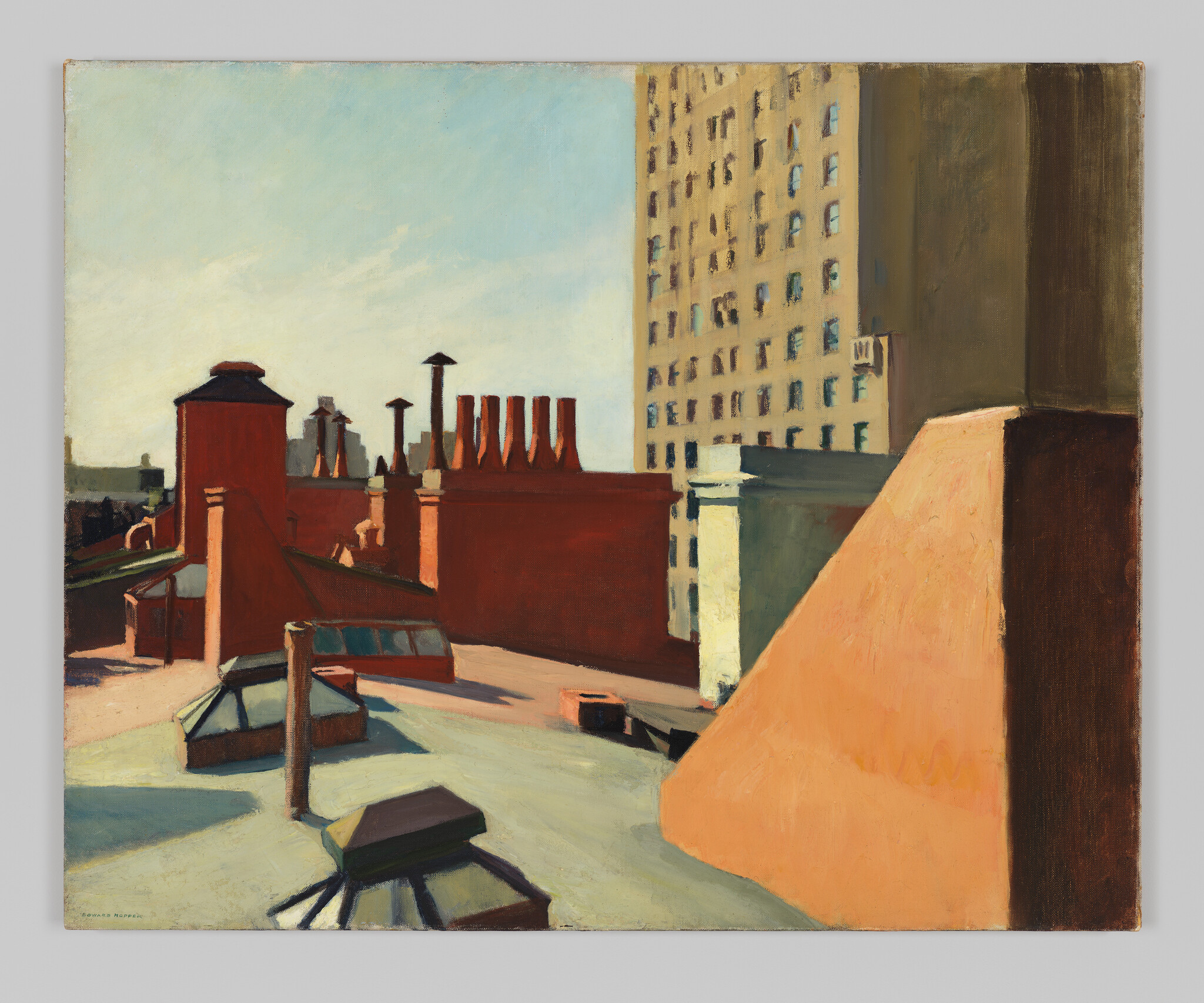 Sunlit city rooftops with chimneys, skylights, and a tall apartment building in the background.