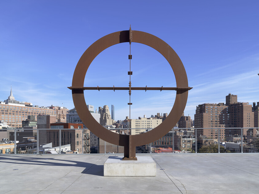 A giant reticle or encircled crosshair made of steel, installed on an open-air terrance backdropped by the cityscape.