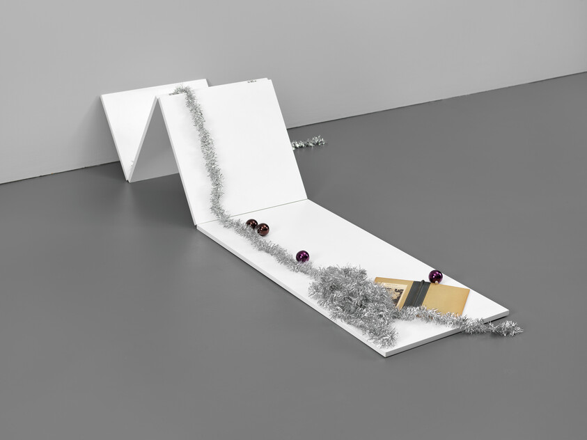 Folded white panels on the floor decorated with silver tinsel, purple ornaments, and a small book.