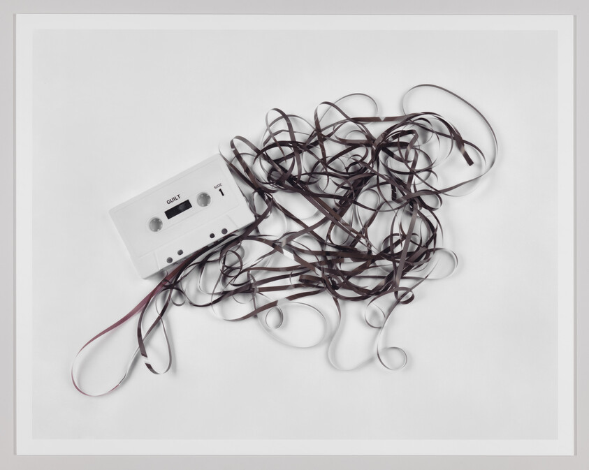 A white cassette tape with unraveled brown tape tangled across a white background.