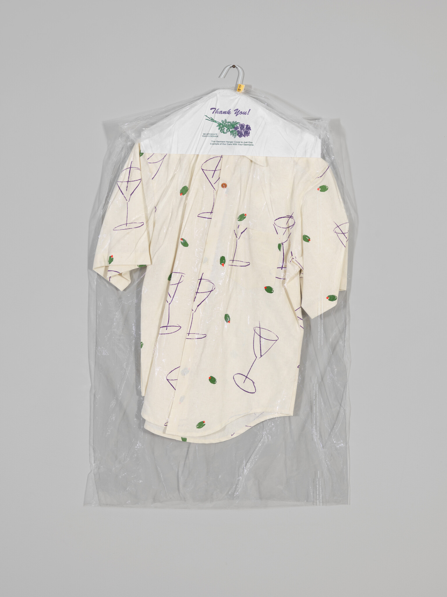 Short-sleeve shirt with martini glass and olive prints hanging in a clear dry-cleaning bag.