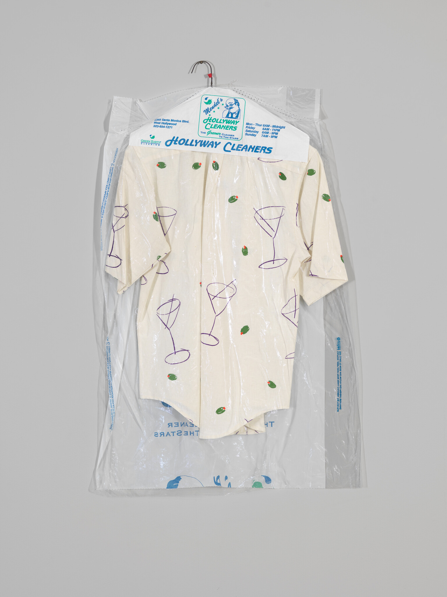 A short-sleeve shirt with cocktail glass prints hanging inside a dry-cleaning plastic bag labeled Hollyway Cleaners.