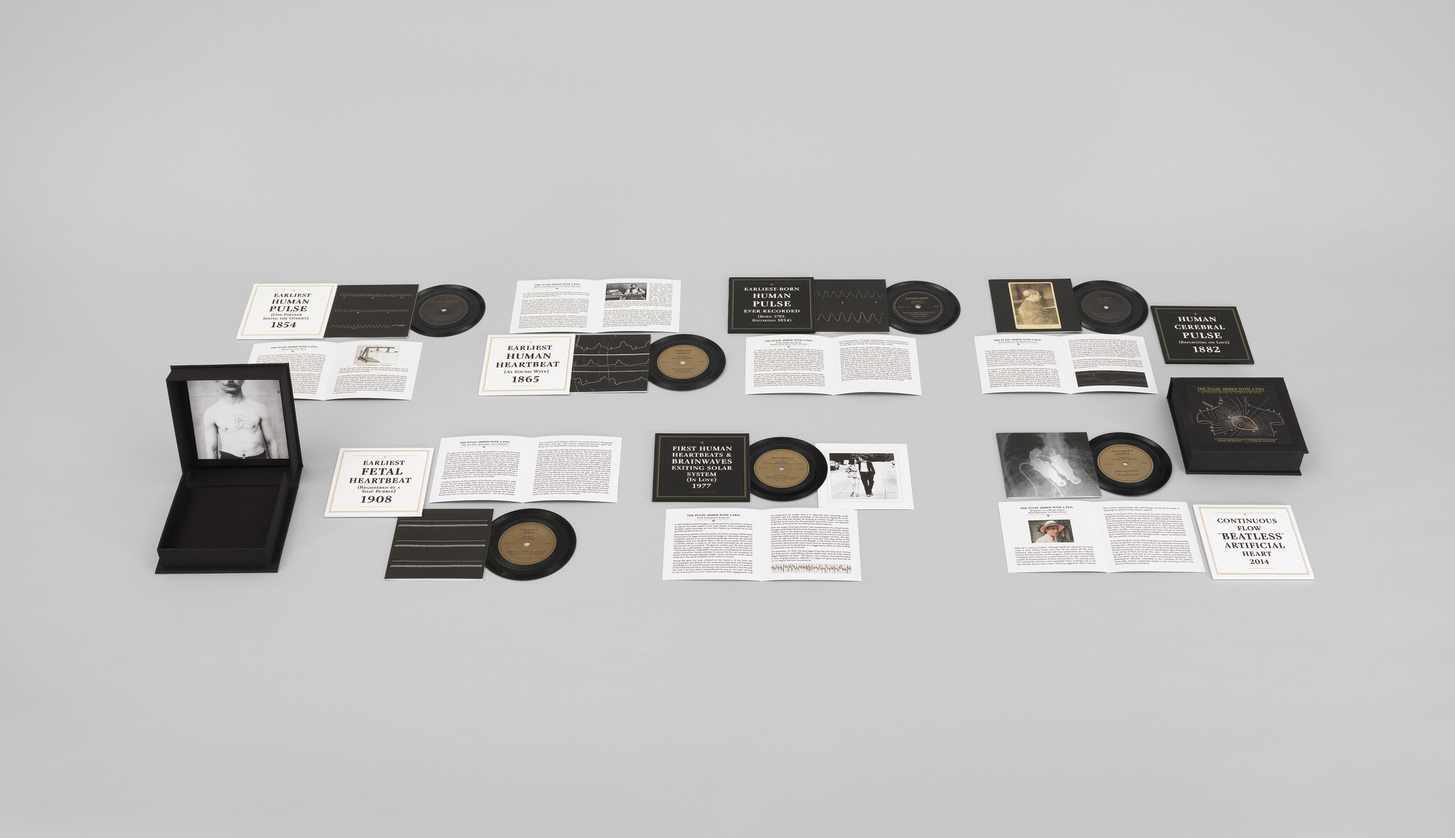 A neat grid of vintage records, booklets, photos, and boxes arranged on a gray surface.