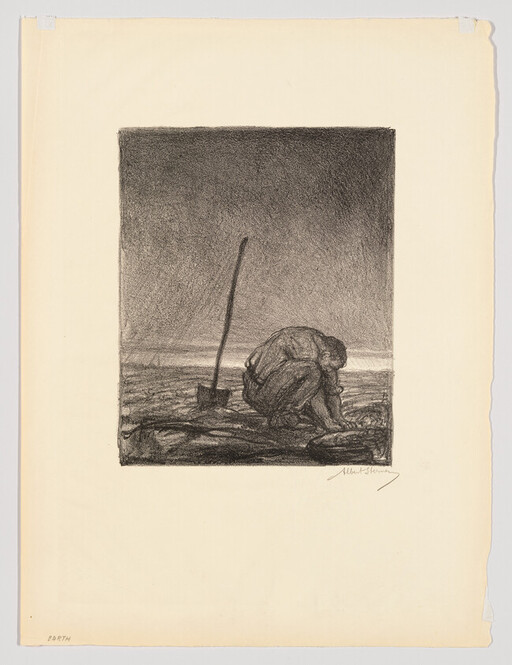 A person crouches on a shoreline next to an upright shovel, looking down at the ground.