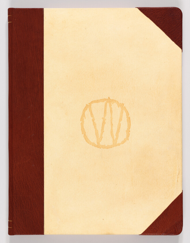 Beige notebook with maroon leather spine and corners and a faded circular monogram in center.