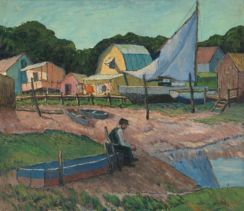 A man sits by a small harbor near beached boats and colorful shacks with a raised sail.