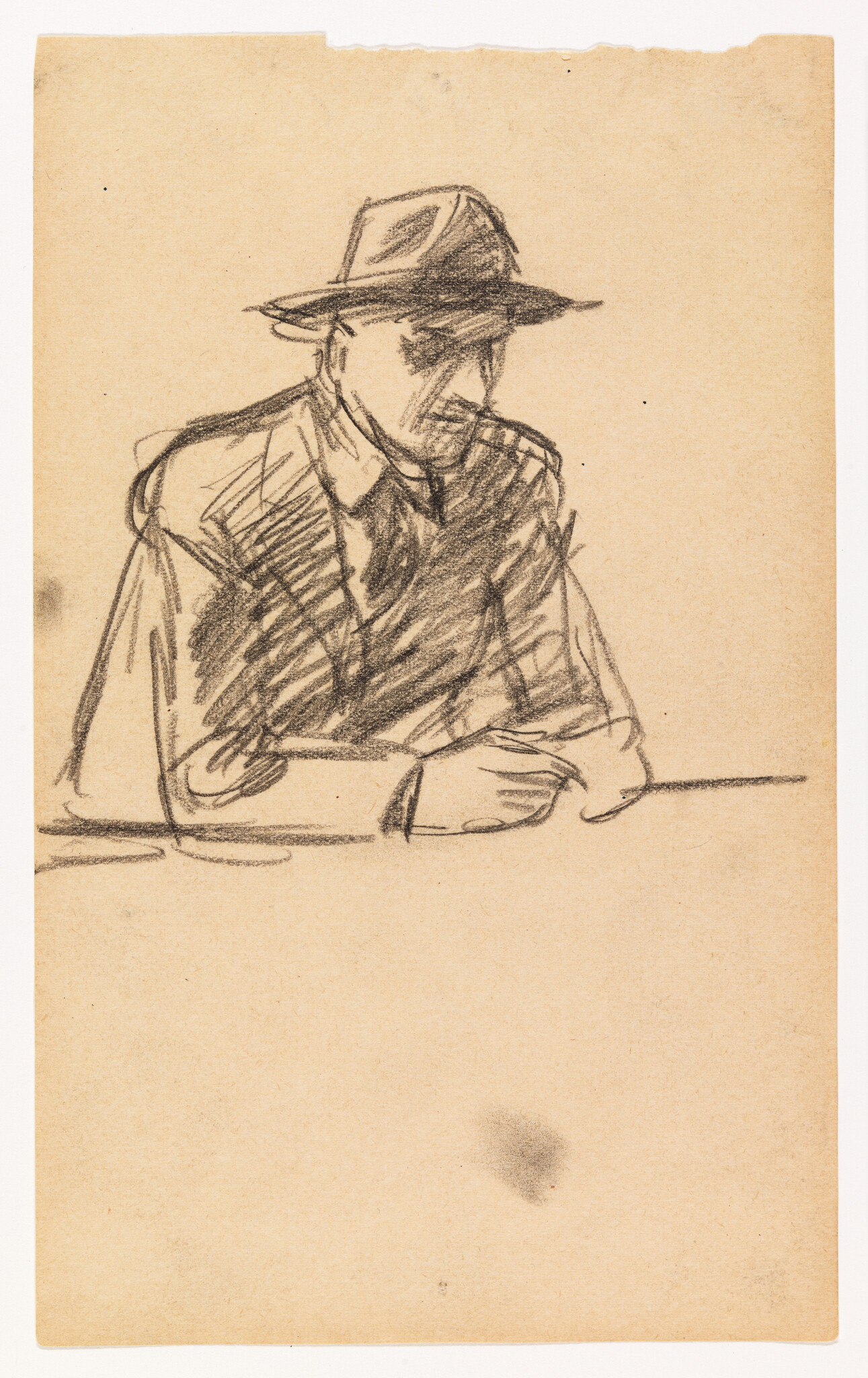 Man wearing a fedora hat sits at a table with hands resting, looking down.