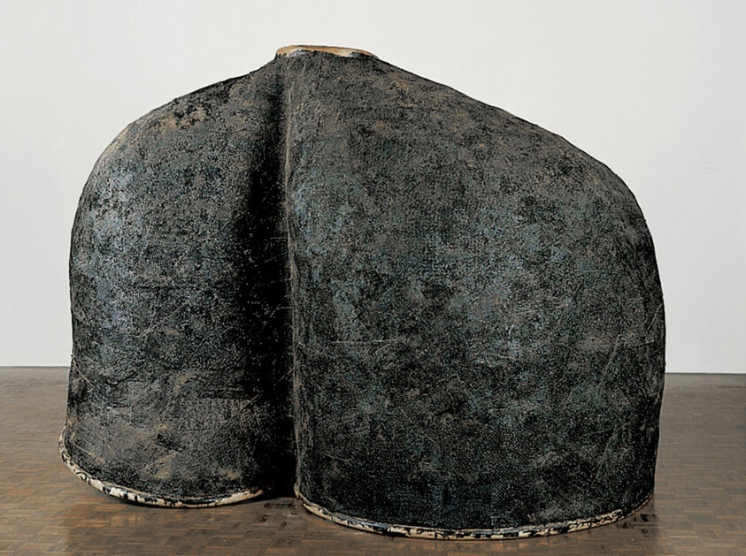 Large dark textured double-bellied sculpture with a visible seam standing on a wooden floor.