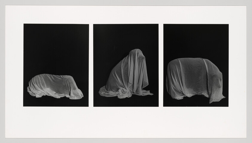 Three black panels show white cloth draped over three shrouded forms suggesting hidden figures.