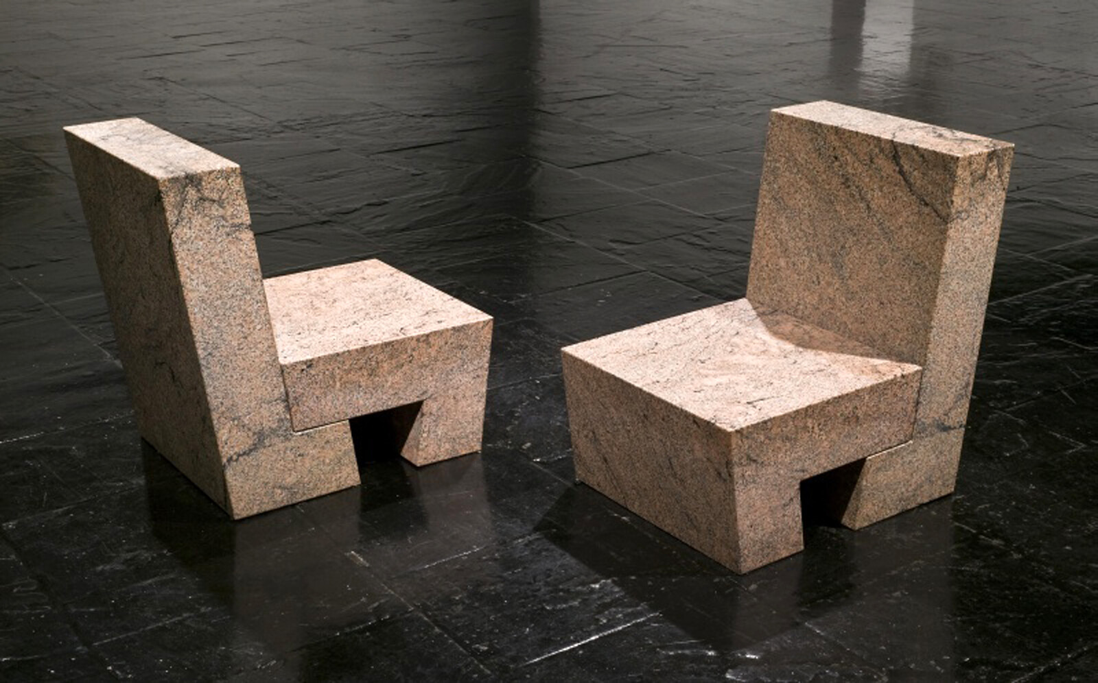 Two blocky stone chairs facing each other on a shiny dark tiled floor.