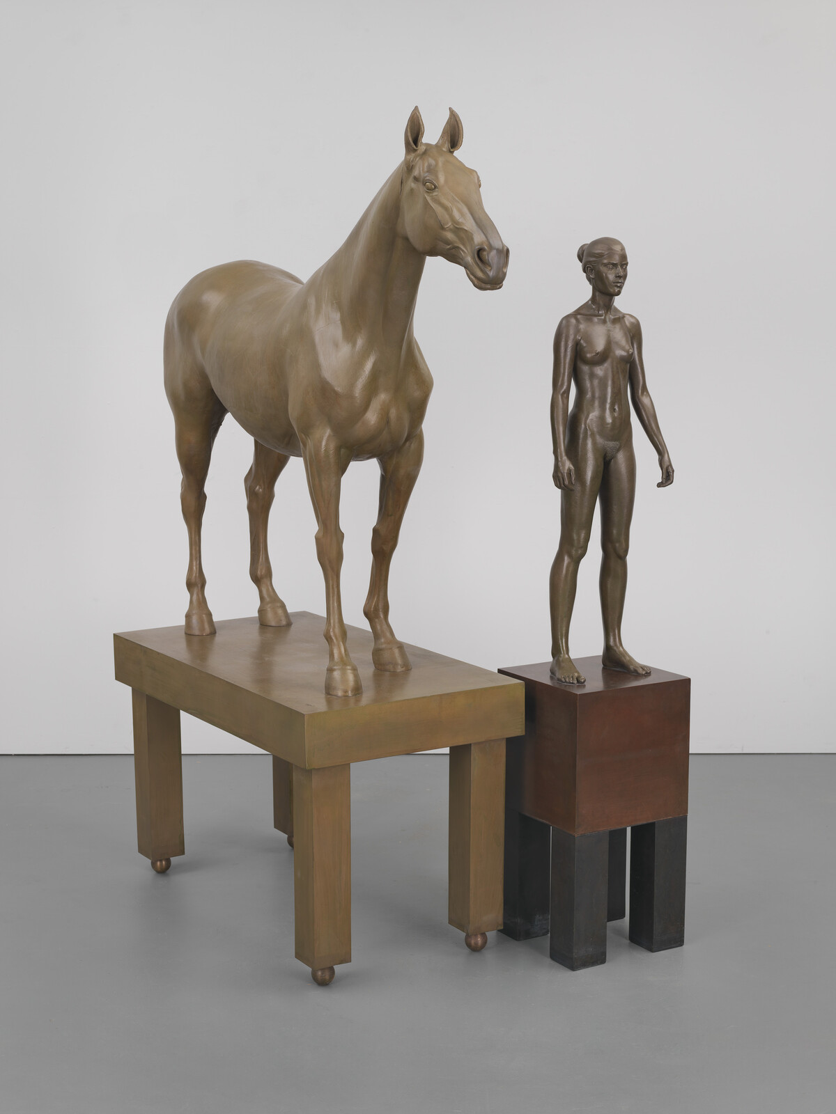 Bronze horse stands on a rectangular table next to a bronze nude woman on a pedestal.