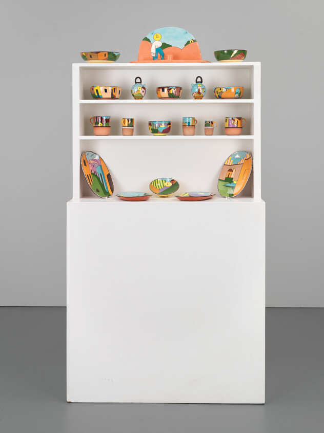 A white shelf displaying colorful hand-painted ceramic bowls and plates on a white pedestal.