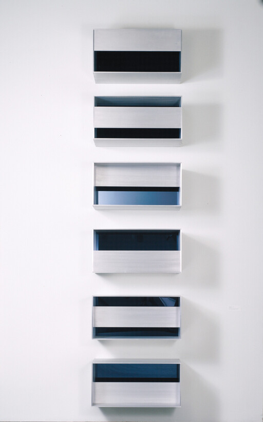 Six rectangular metal wall boxes with dark horizontal window bands arranged vertically on a white wall.