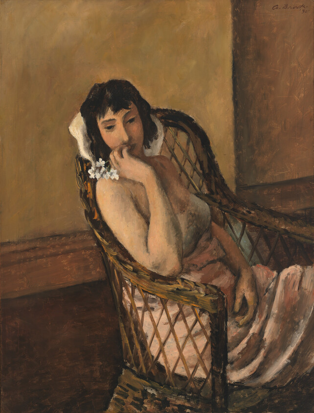 A woman sits in a wicker chair holding small white flowers and resting her chin on her hand.