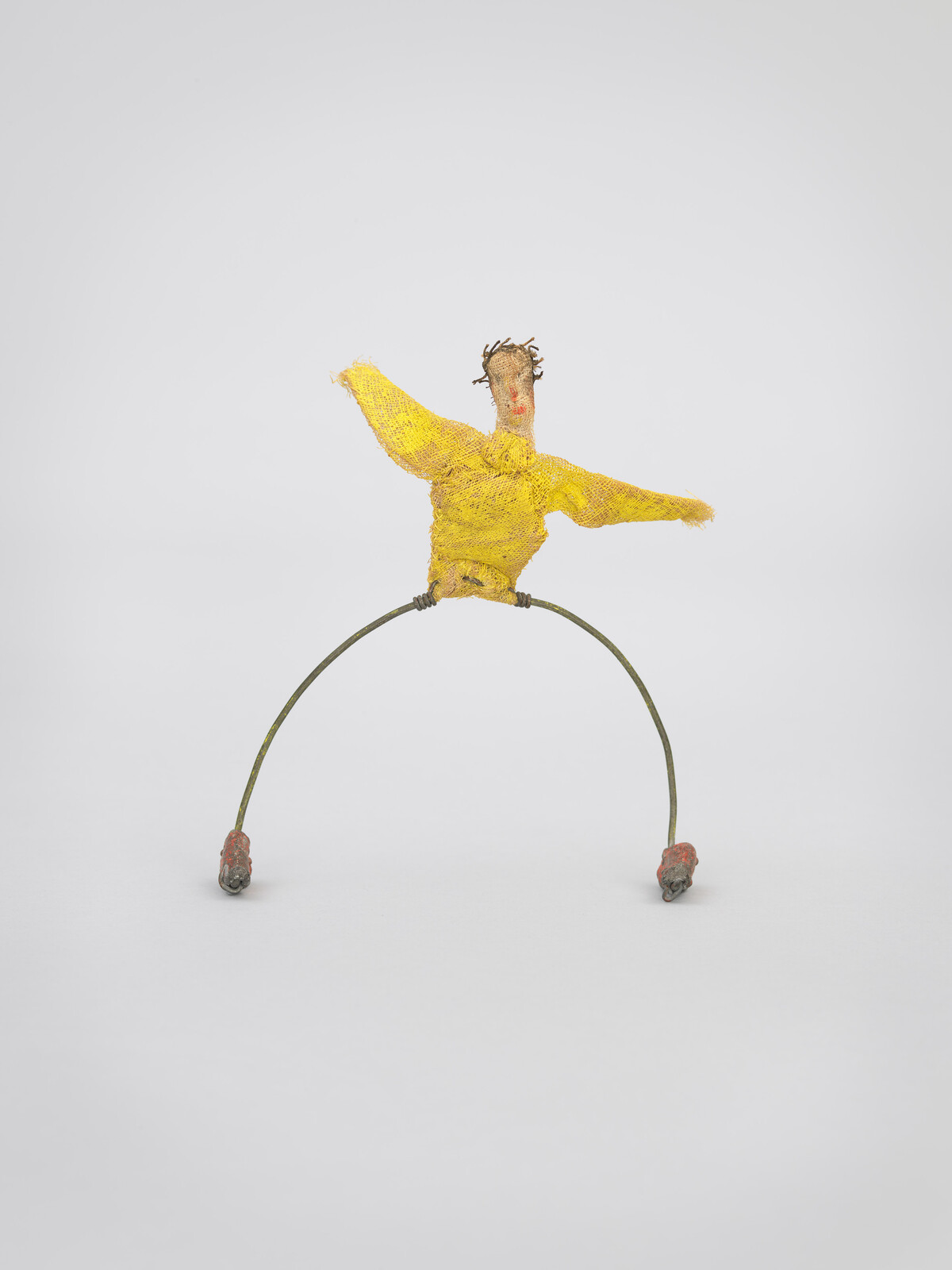 A small wire sculpture of a person with a yellow shirt and outstretched arms.
