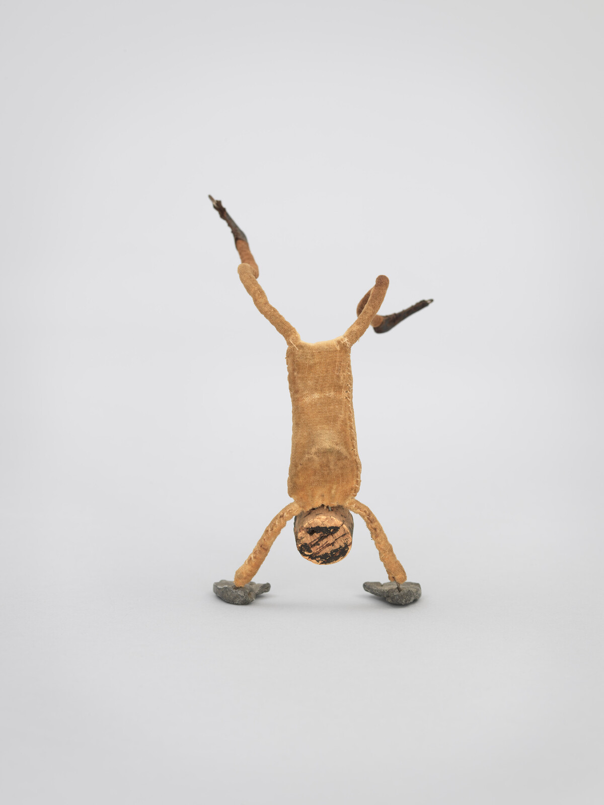 A small, abstract figure made of natural materials performs a handstand on a plain background.