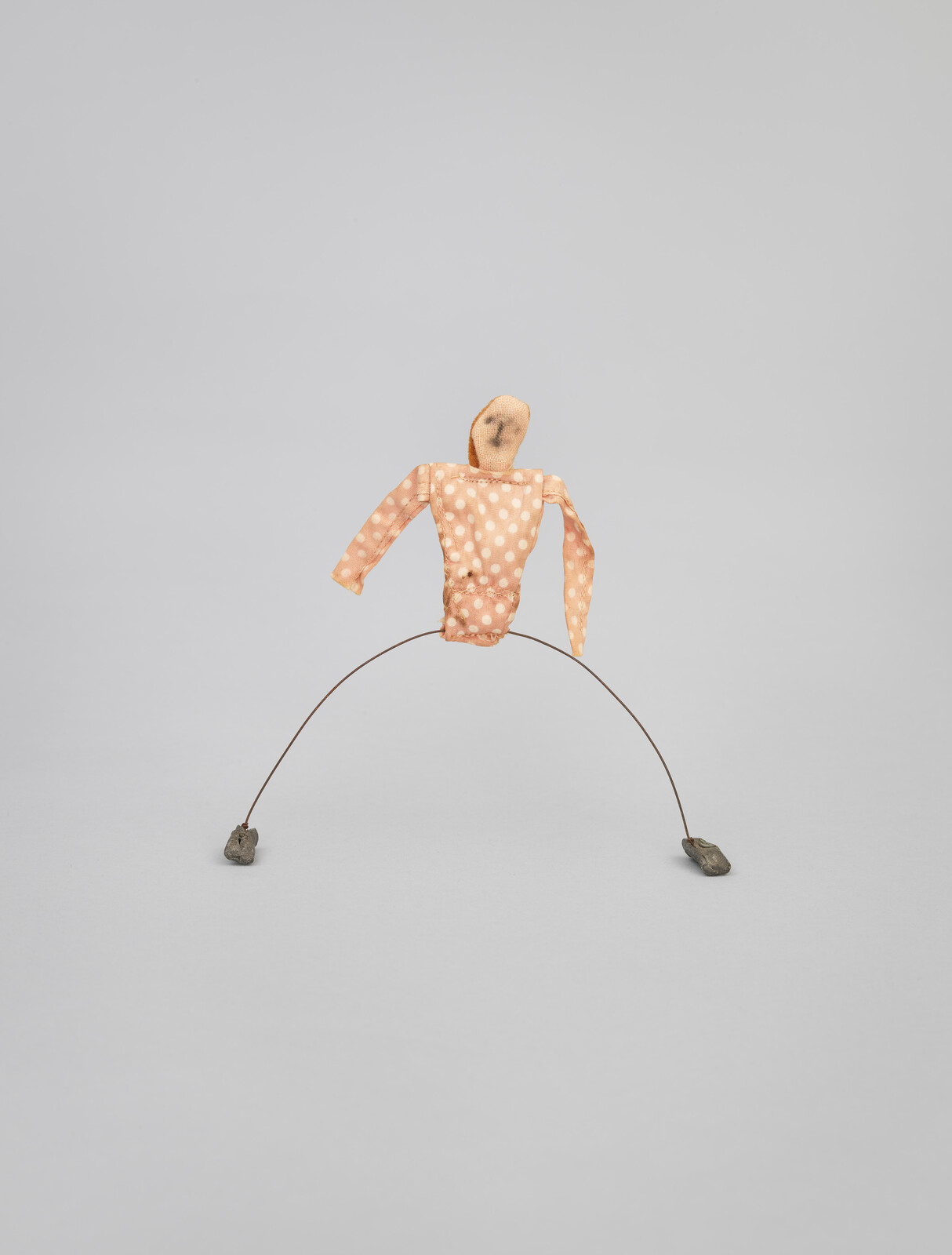 Small wire sculpture with a polka dot fabric torso and stone feet on a plain background.