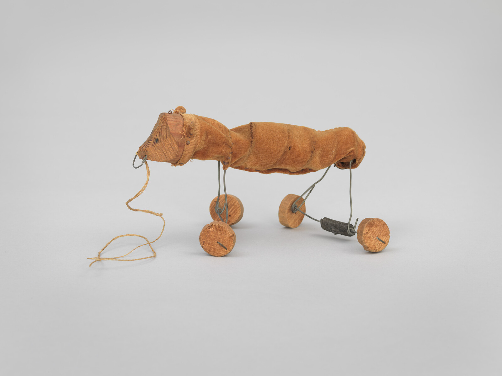 A vintage toy horse with a fabric body, wooden wheels, and a string attached to its head.