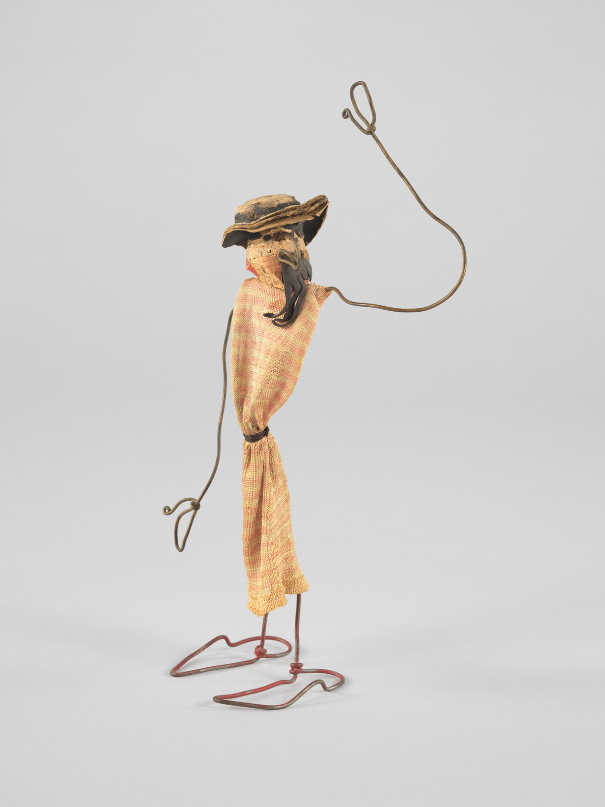 Wire sculpture of a person with a hat, wearing a cloth, raising one arm.