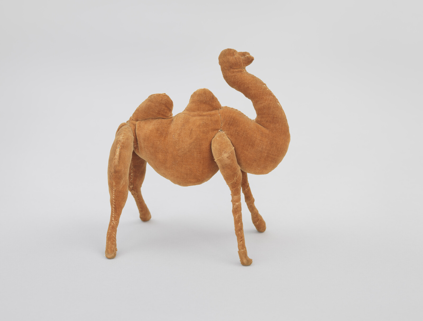 A small brown two-hump stuffed camel toy standing on a plain light background.