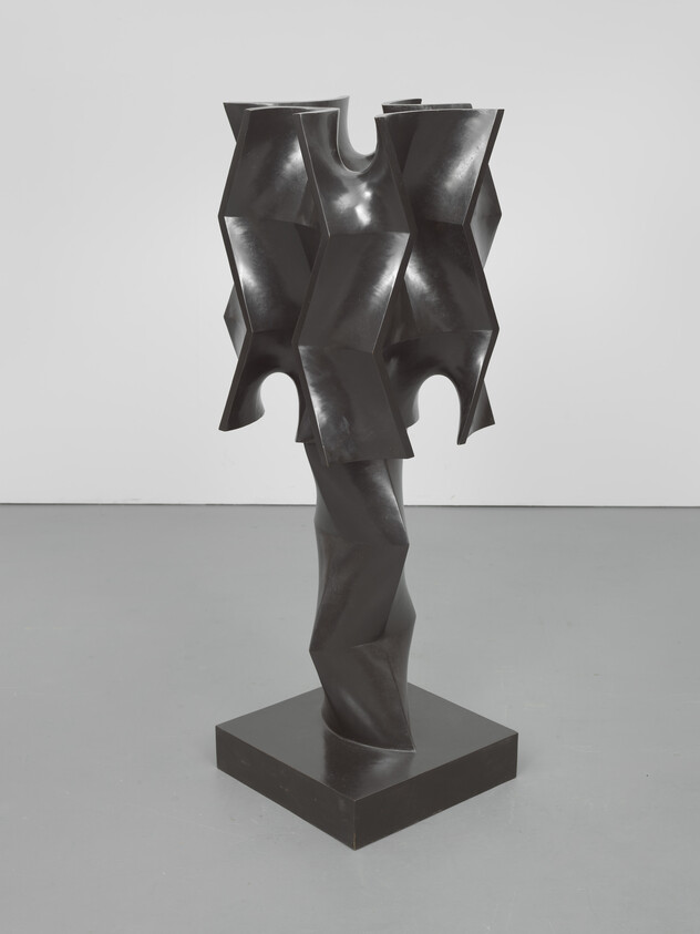 Black geometric metal sculpture with stacked hexagonal forms on a twisted pedestal in a gallery.