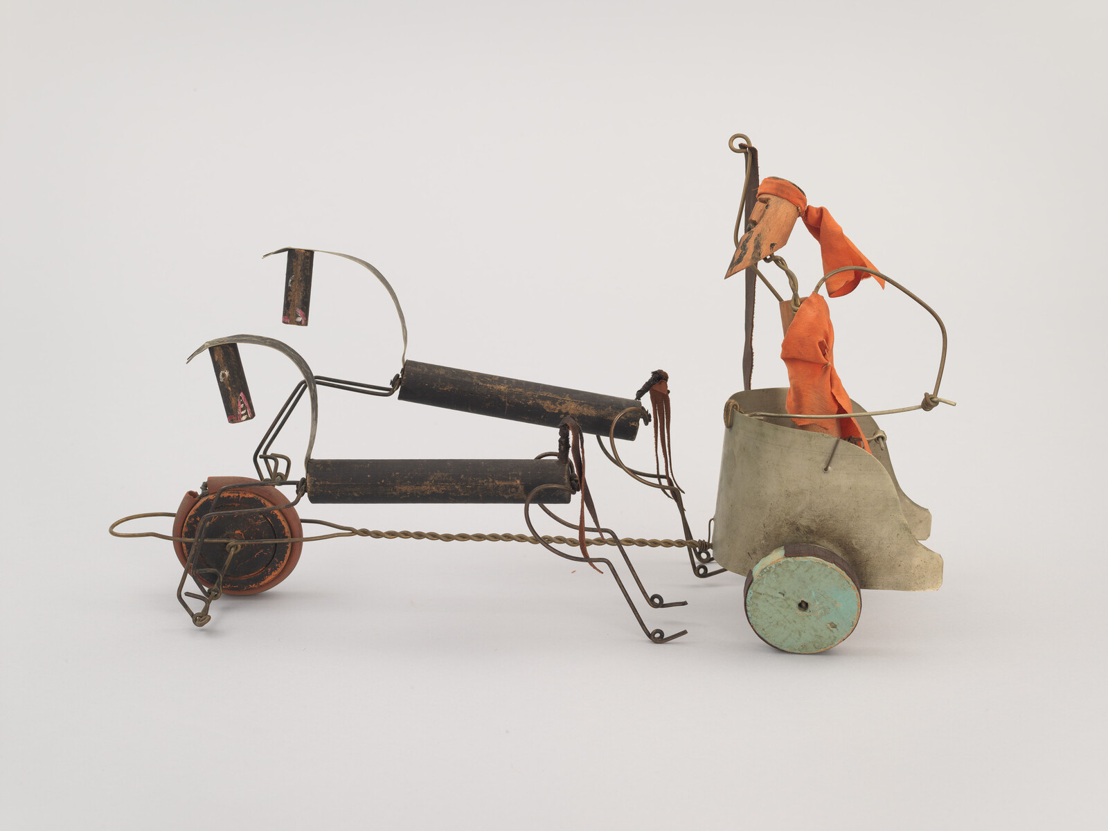 A small wire and metal toy cart pulled by a wire frame with orange-clothed figure.