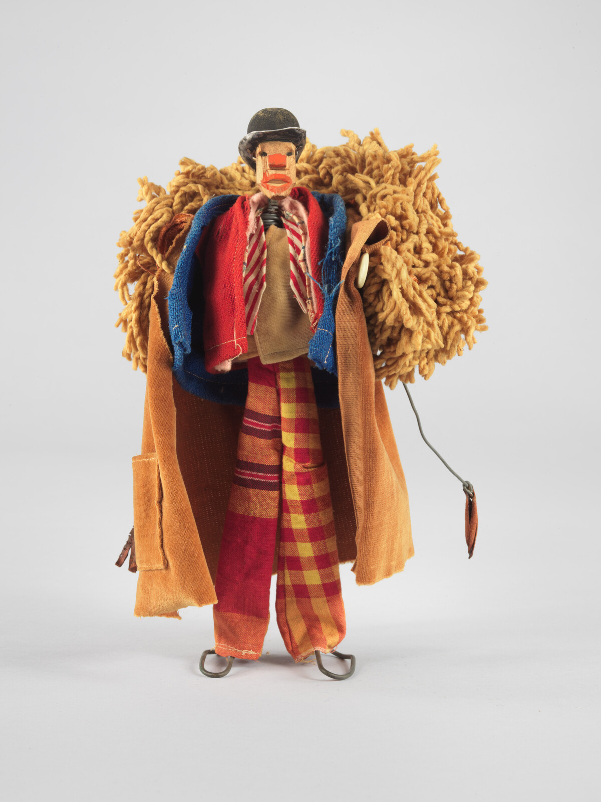 Wooden puppet clown wearing colorful coat and plaid pants with fluffy yellow backpiece.