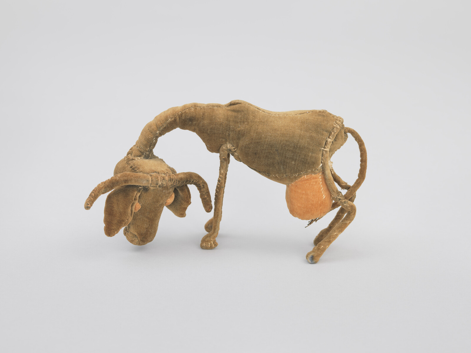 Worn brown stuffed animal with curved horns and stitched limbs standing with head lowered.