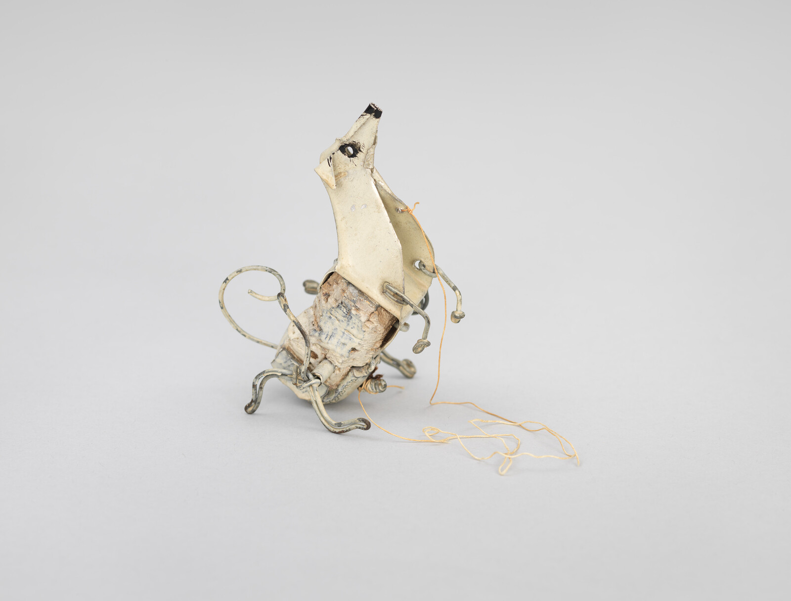 A small wire-and-metal animal sculpture with bent legs and loose thread trailing behind it.