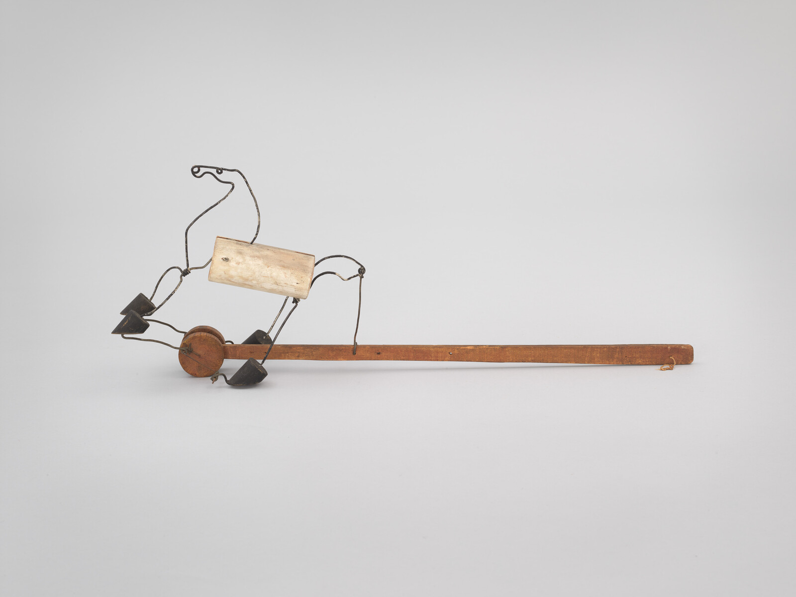 A simple wooden stick with wire-framed horse puppet, small wheel and attached weights.