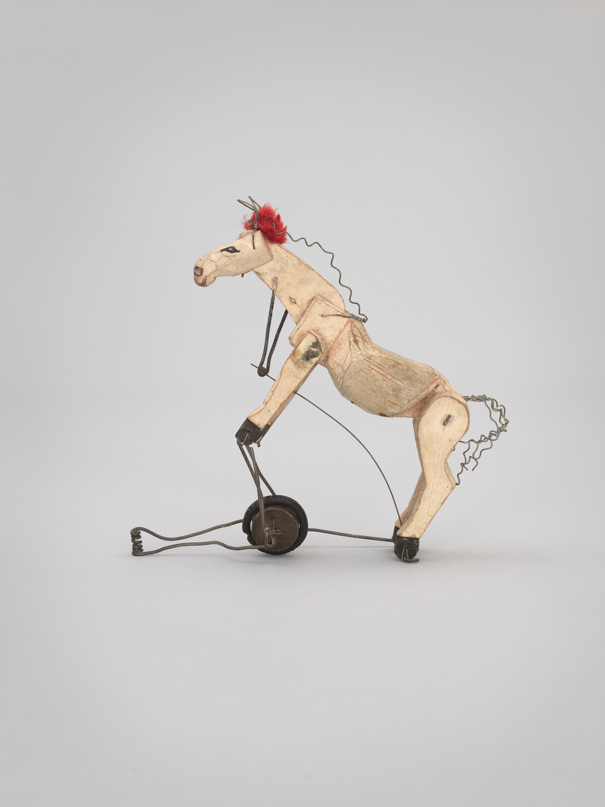 A small wooden toy horse with wire wheels and a red tuft on its head.