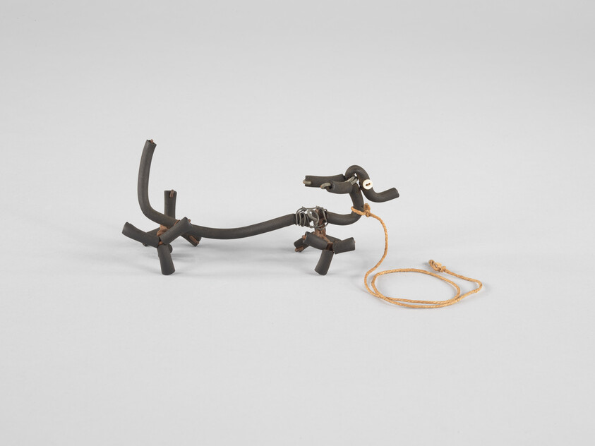 Small dog sculpture made from black rubber tubing with a coiled rope leash attached.