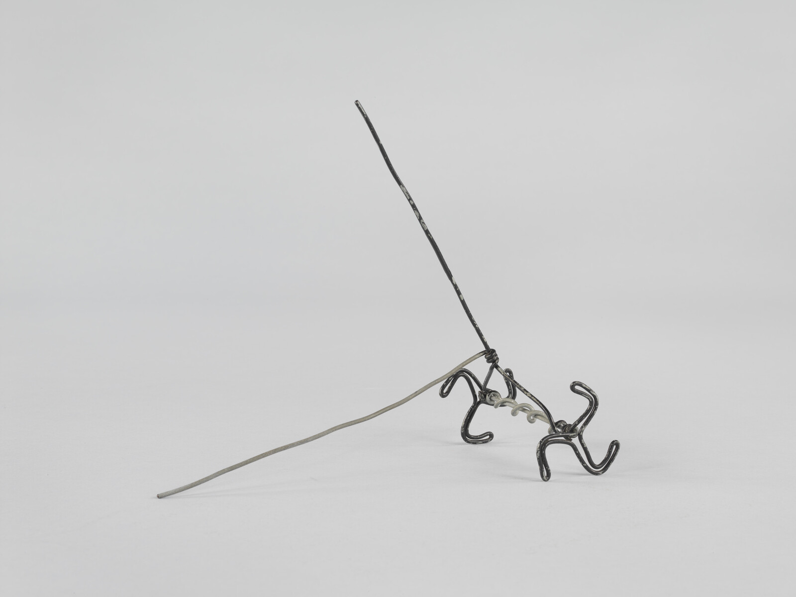 Small twisted wire sculpture with looped legs and two long thin rod-like extensions.