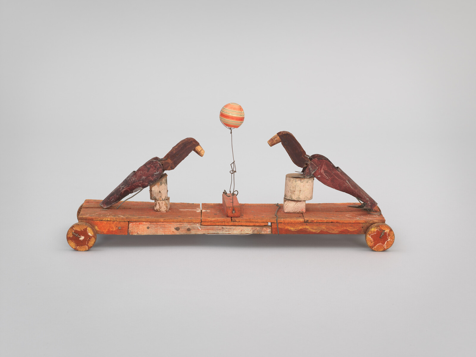 Wooden toy with two bird figures on a wheeled base and a striped ball.