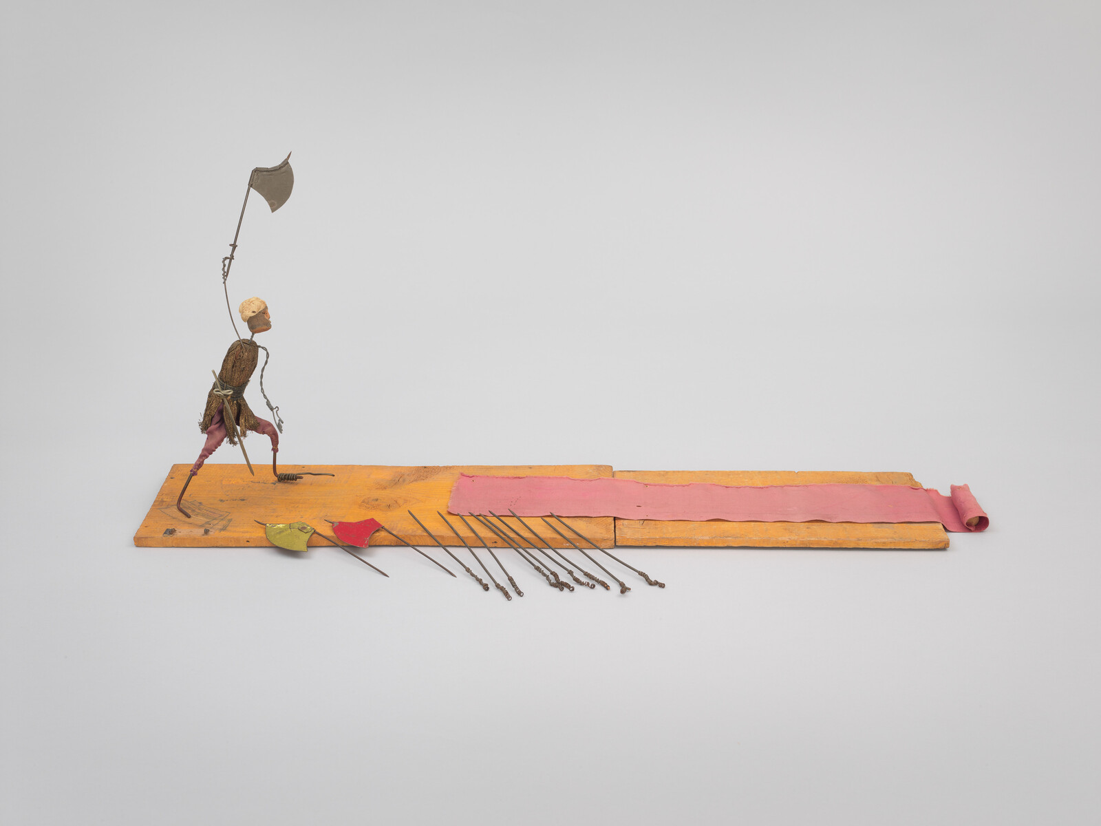A wire-and-wood figure strides on a wooden board while holding a raised axe-like flag.