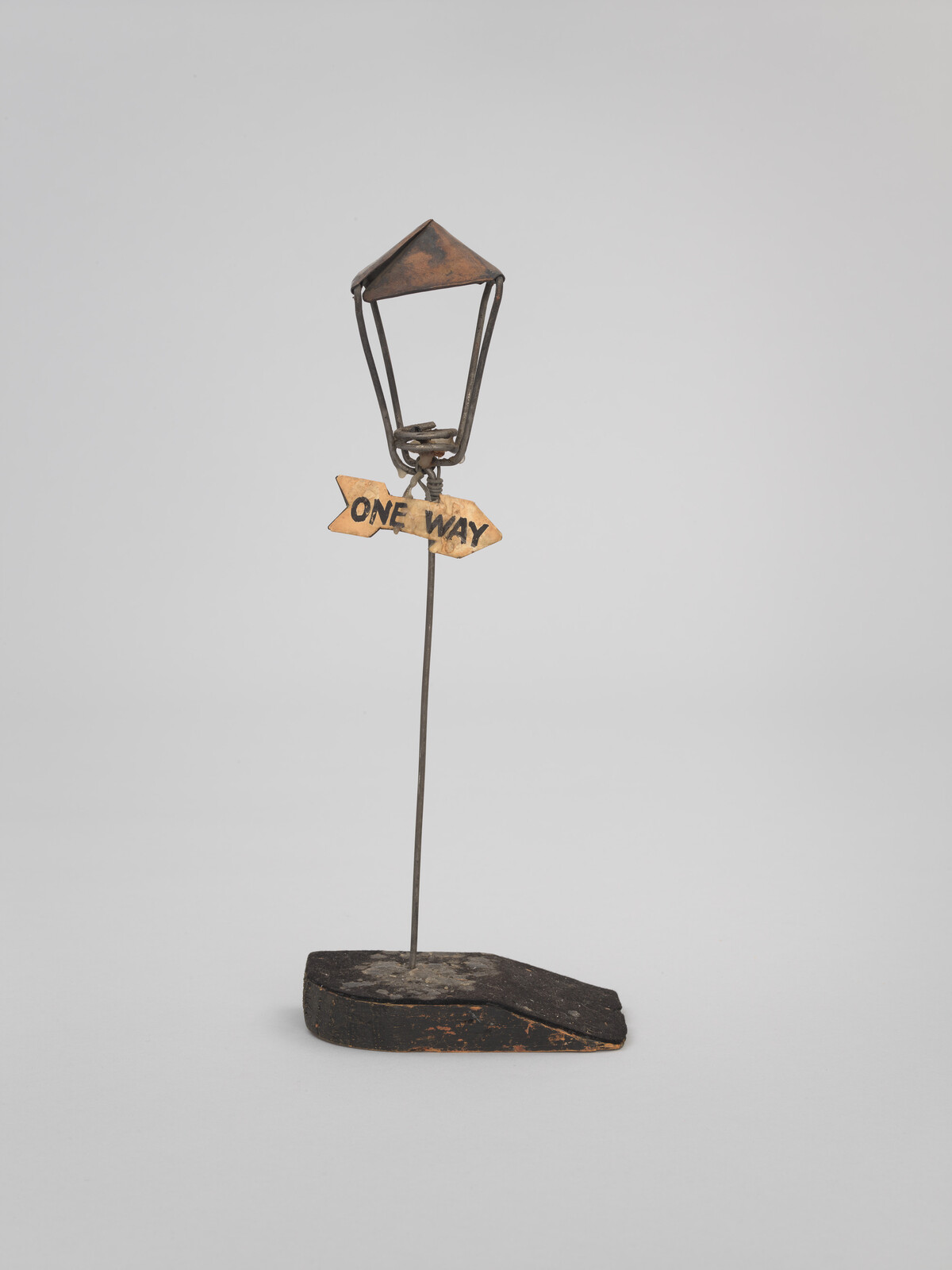 Small metal lamp post sculpture with a one-way arrow sign mounted on a wooden base.