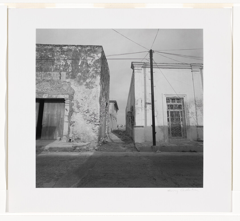 Two weathered buildings flank a narrow alley with a utility pole and overhead wires.