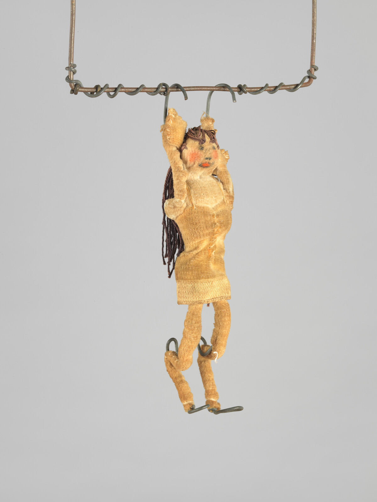 A small cloth doll with yarn hair hangs by its hands from a twisted metal wire.