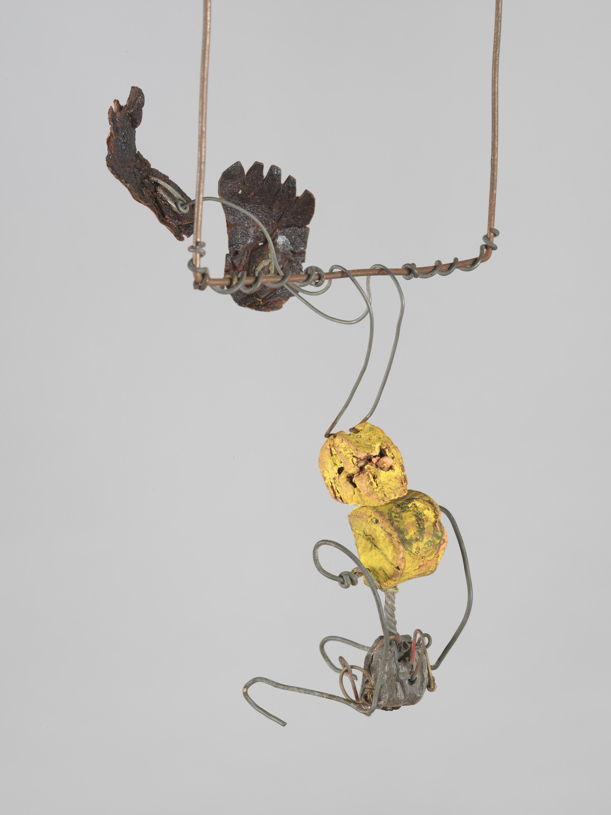 A hanging wire sculpture with two yellow painted clay pieces suspended from a twisted metal frame.