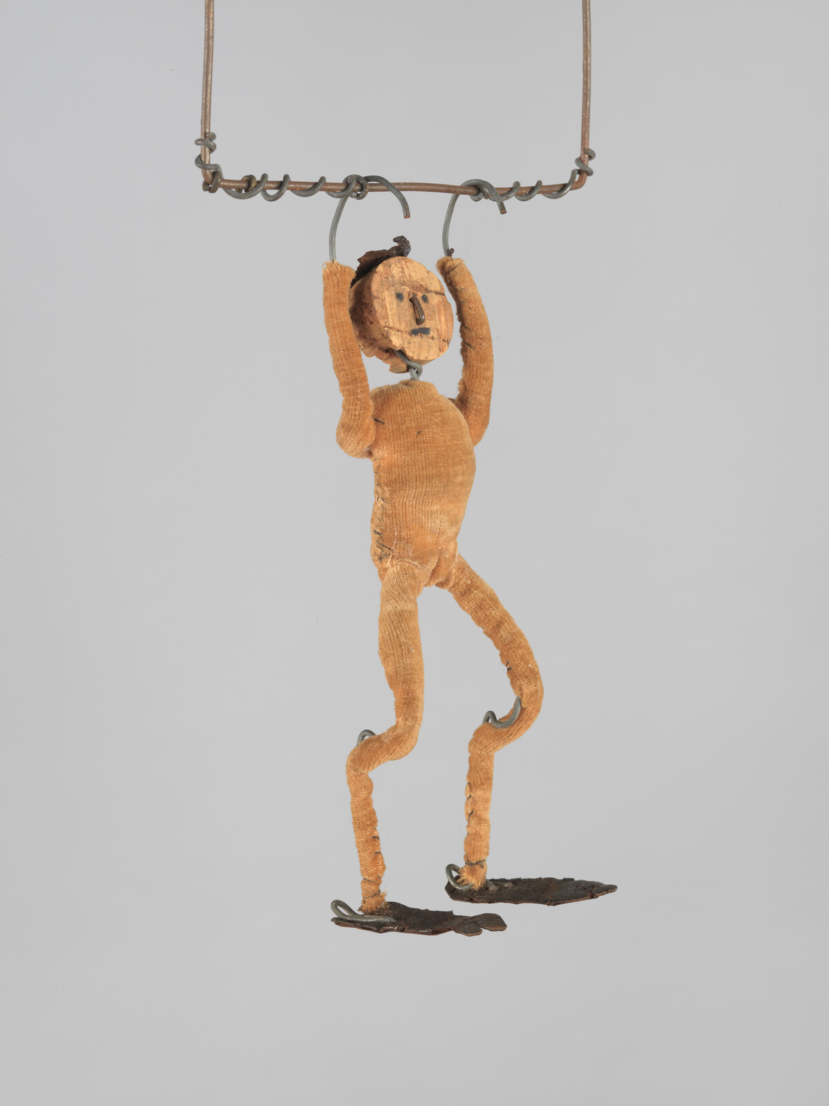 A worn cloth and wire marionette hangs by its hands from a twisted metal bar.