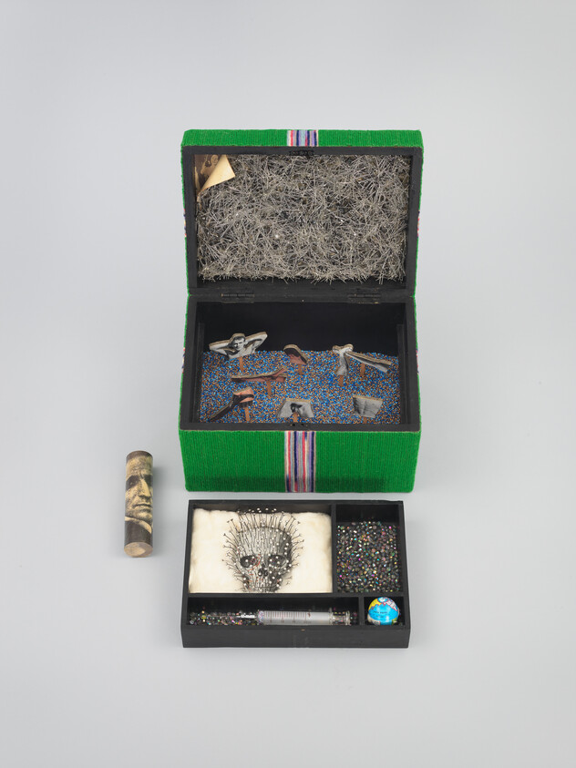 Open green beaded box with tray holding pin-filled skull, beads, tiny globe, and vial.