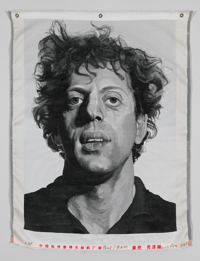 A grayscale portrait of a man with curly hair on a fabric canvas, featuring Chinese characters and English text along the bottom edge, with metal grommets at the corners for hanging.