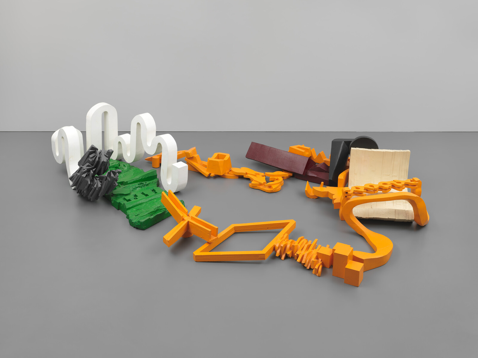 Colorful abstract interlocking sculptures in white, green, orange, and maroon lying on a gray floor.