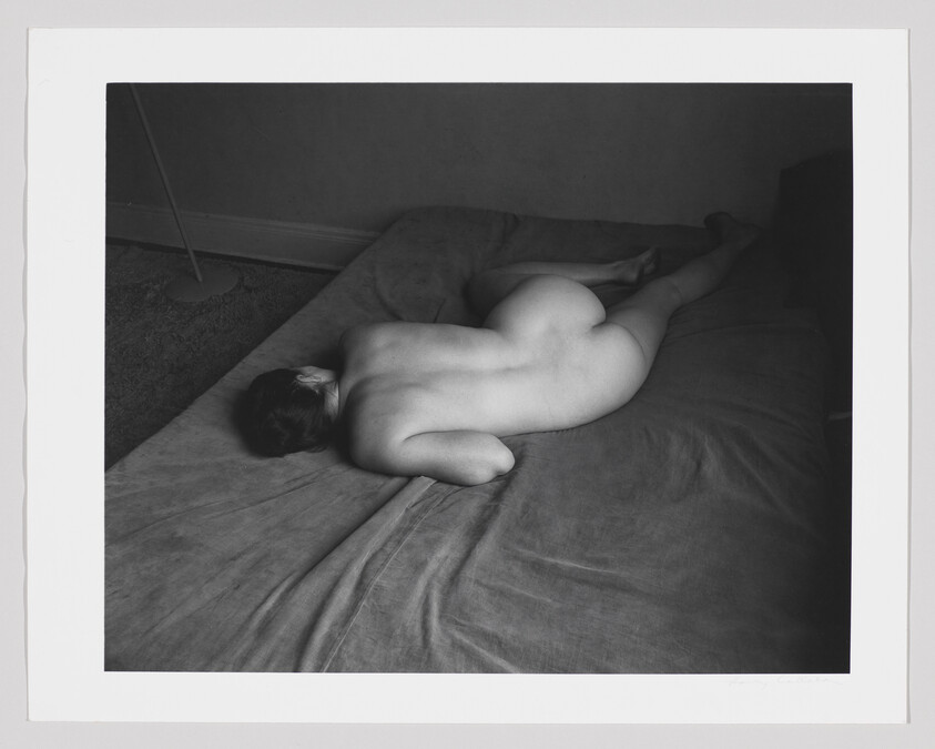 Naked person lying face down on a bed with one arm tucked under their body.
