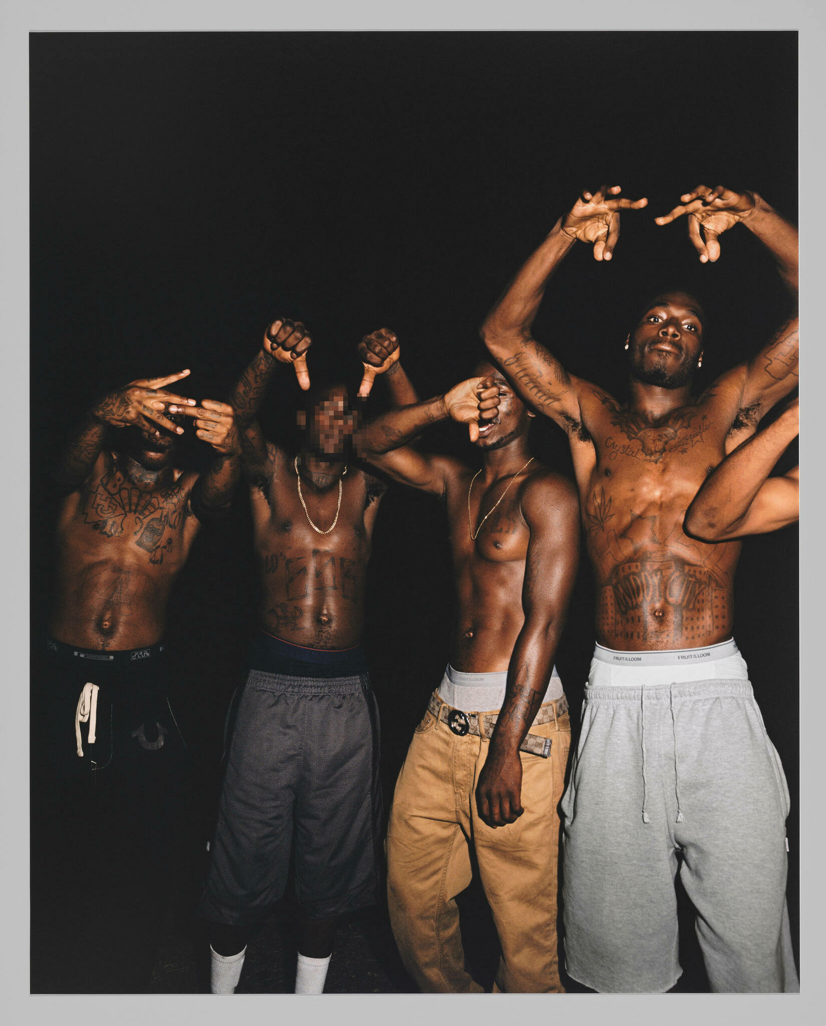 Four standing and shirtless Black men facing and signing at the photographer against a black background. One man's face is blurred.