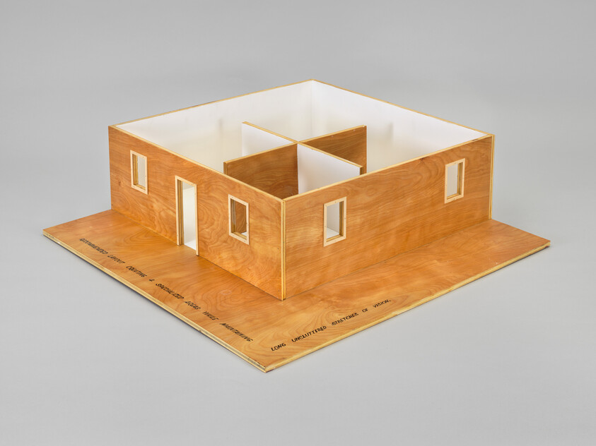 A simple wooden architectural model showing a one-story house shell with interior partition walls and window openings.