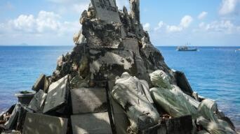 A large pile of broken concrete slabs and statues piled on the rocky shore by the ocean.
